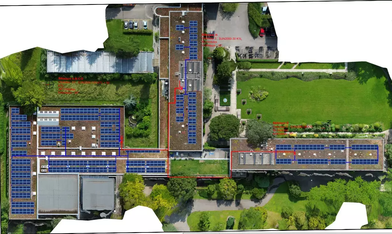 Vue aérienne schématique du site présentant l’implantation des panneaux photovoltaïques sur plusieurs toitures, avec le tracé des câbles et des onduleurs indiqués en rouge et en bleu. 