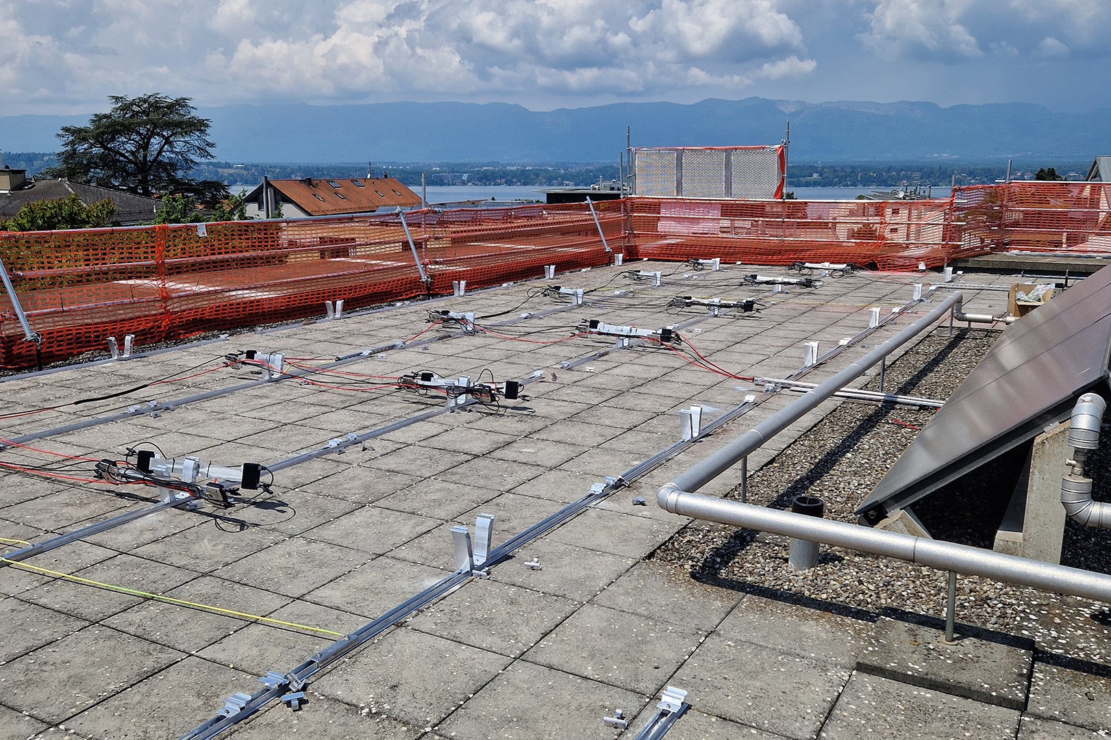 Installation du système de fixation pour panneaux solaires sur le toit plat d’un immeuble résidentiel à Vésenaz, avec vue sur le lac Léman et le jura en arrière-plan.