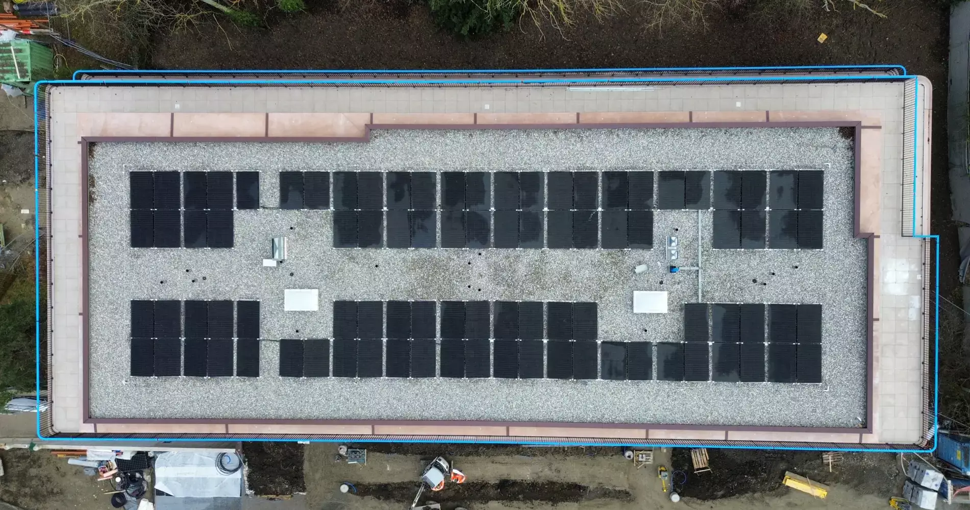 Panneaux photovoltaïques posés sur une toiture plate en gravier, avec garde-corps de sécurité et vue sur des immeubles résidentiels en arrière-plan.