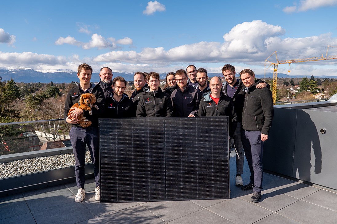 Photo de l’équipe tera solar réunie autour d’un module photovoltaïque, sur le toit-terrasse des bureaux avec Genève en arrière-plan.