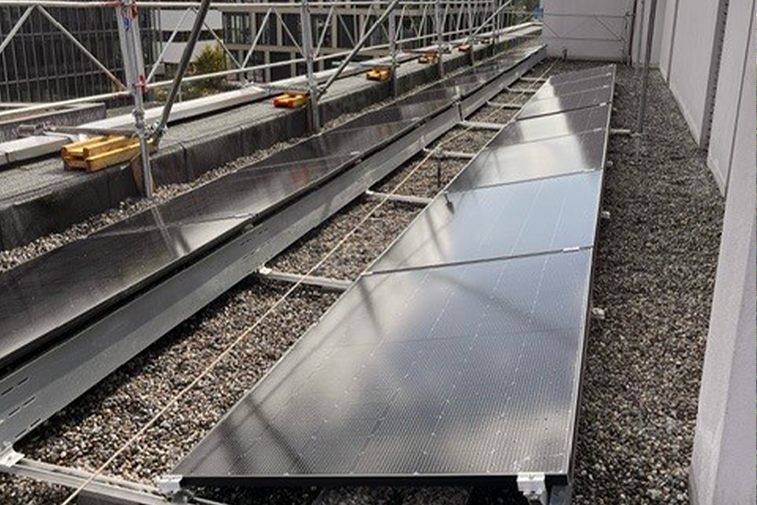 Photo de l’immeuble résidentiel à Meyrin pendant les travaux avec plusieurs panneaux photovoltaïques déjà posés sur la toiture en gravier.