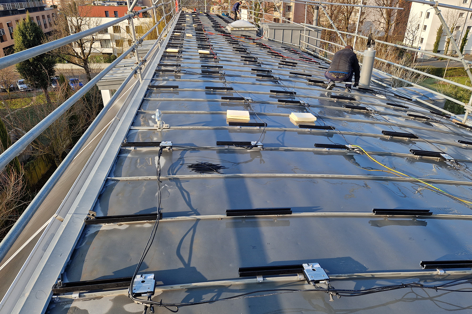 Montage de rails sur une toiture en pente pour l’installation de panneaux photovoltaïques, avec deux techniciens en action.