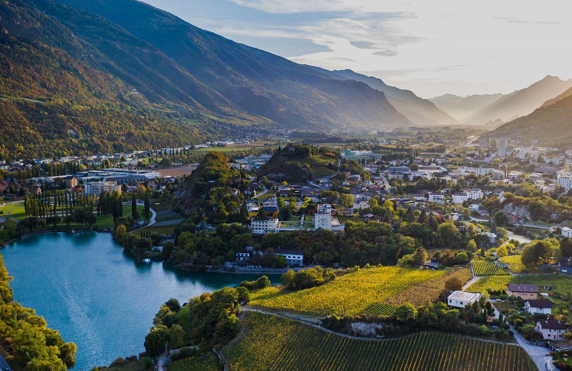 Vue aérienne de la région de Sierre en Valais avec lac, vignes et habitations, illustrant le potentiel solaire de la Suisse romande.